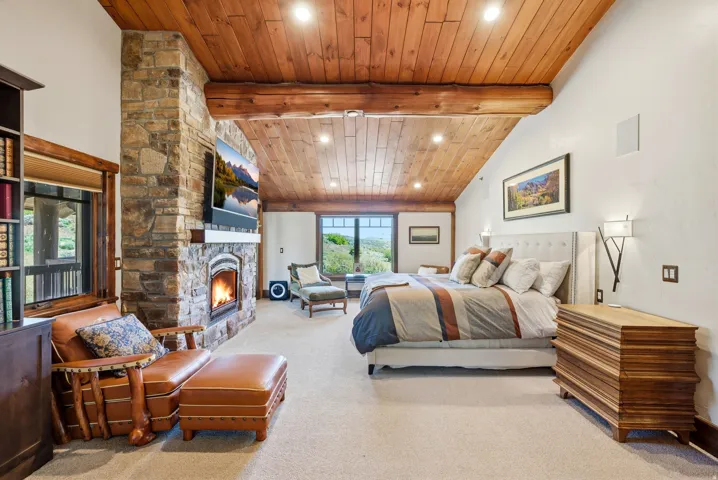 Vaulted wood-paneled ceiling with exposed beams, stone fireplace, and built-in shelving