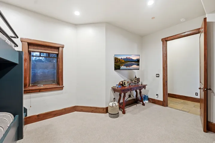Recessed lighting illuminates a carpeted room featuring a built-in bunk bed structure and a window with wood-finish trim