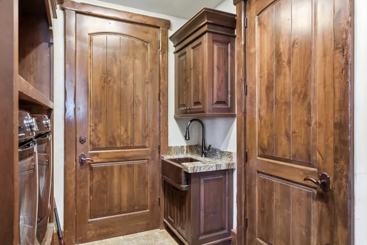 Laundry area featuring custom wood cabinetry, a built-in utility sink with a dark bronze faucet, and stone countertop
