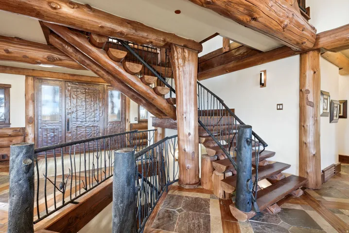 Log-beamed staircase featuring custom wrought iron railings with tree branch details and wood-finish treads