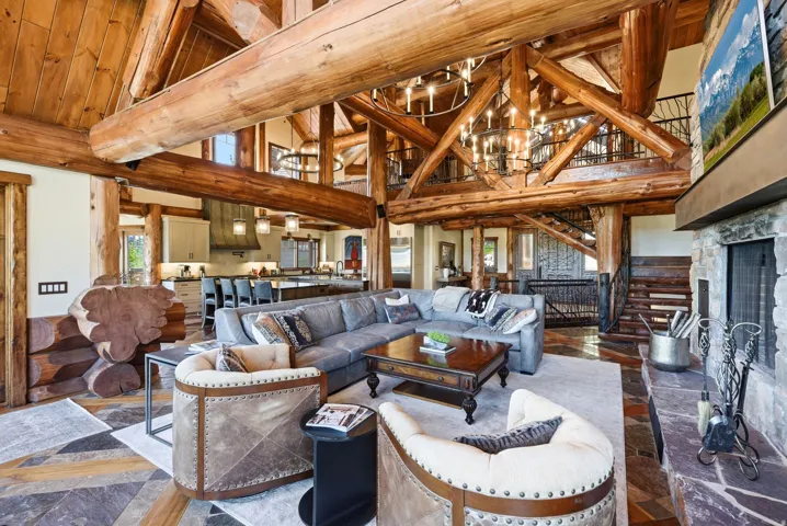 Expansive living area featuring exposed log beams, a stone fireplace, and mixed-material flooring
