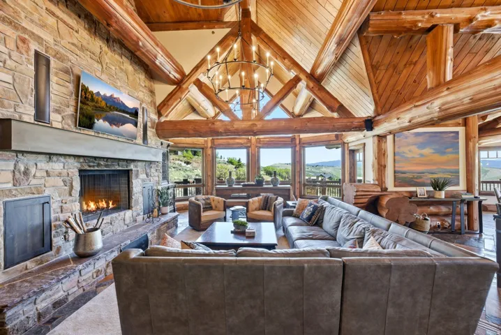 Expansive living area showcasing a vaulted wood-beam ceiling, a large stone fireplace with a substantial hearth, and multiple windows