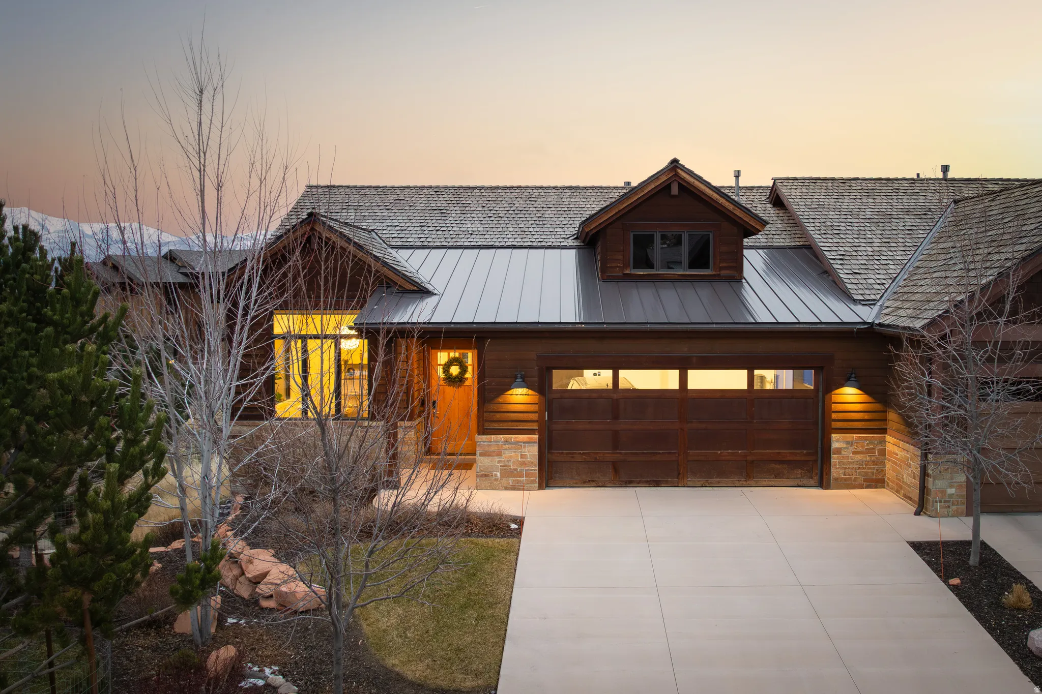 View of front of house featuring stone siding, concrete driveway, a garage, and a metal roof