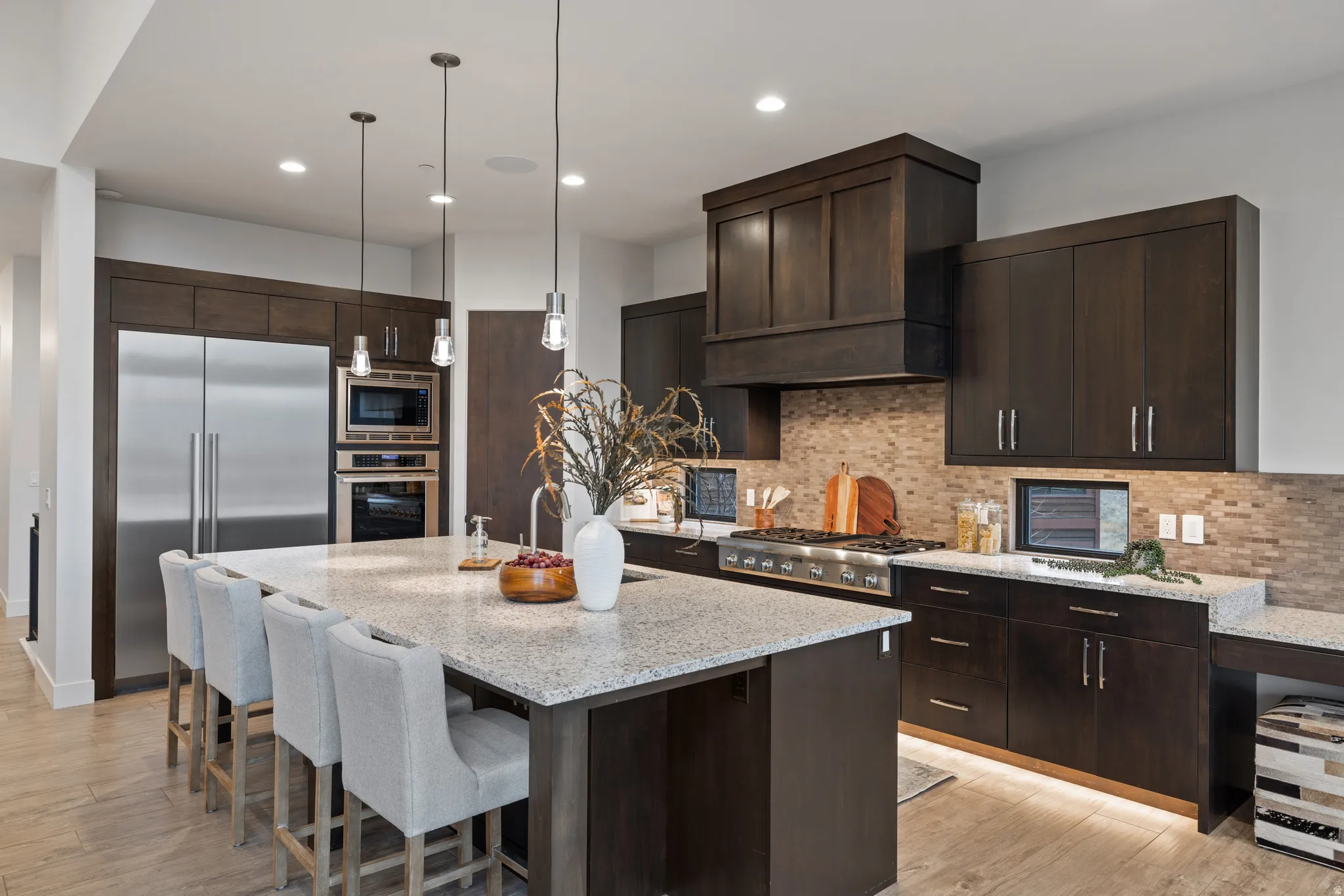 Kitchen with dark brown cabinetry, light stone counters, built in appliances, and recessed lighting