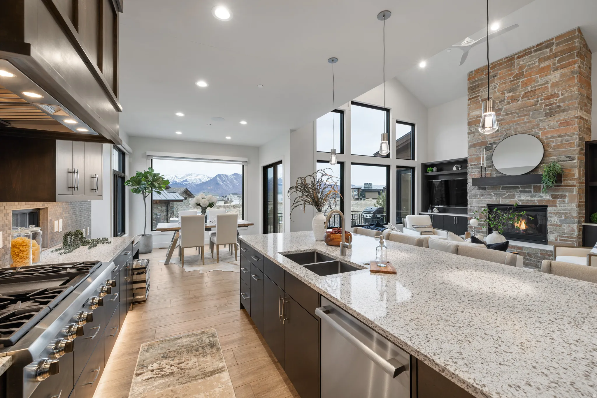 Kitchen with light stone countertops, stainless steel appliances, exhaust hood, hanging light fixtures, and high vaulted ceiling