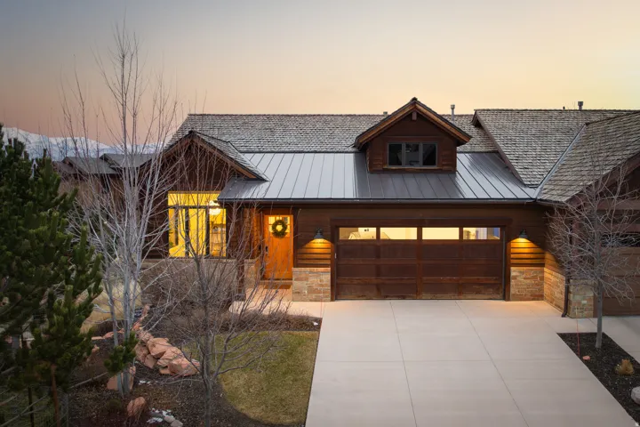 View of front of house featuring stone siding, concrete driveway, a garage, and a metal roof