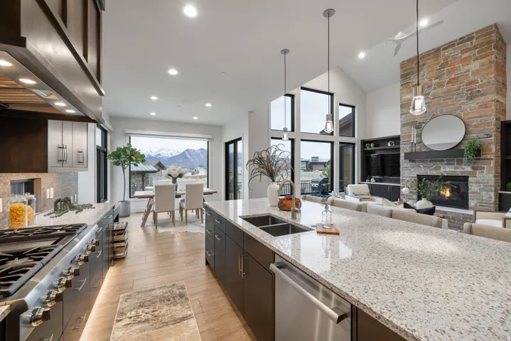 Kitchen with light stone countertops, stainless steel appliances, exhaust hood, hanging light fixtures, and high vaulted ceiling
