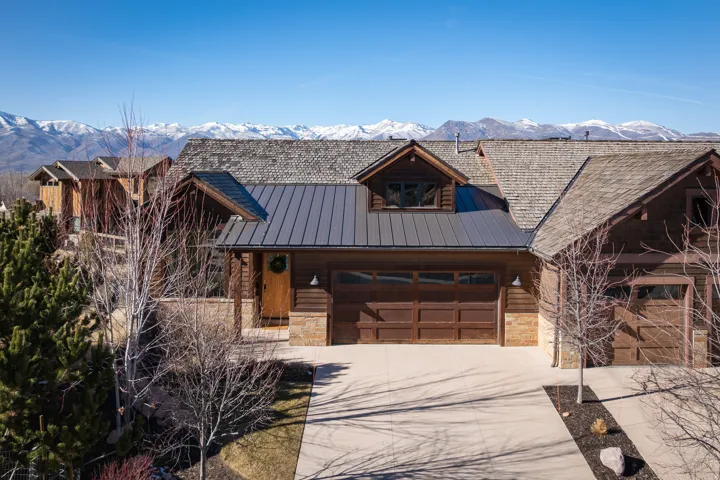 Log-style house featuring stone siding, a garage, and driveway
