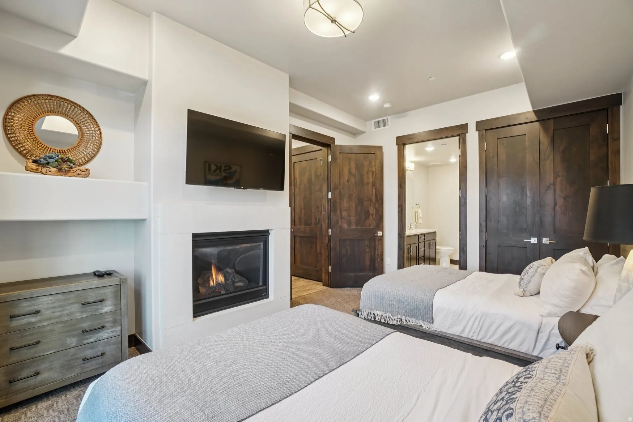 Bedroom with a glass covered fireplace, ensuite bathroom, and light colored carpet