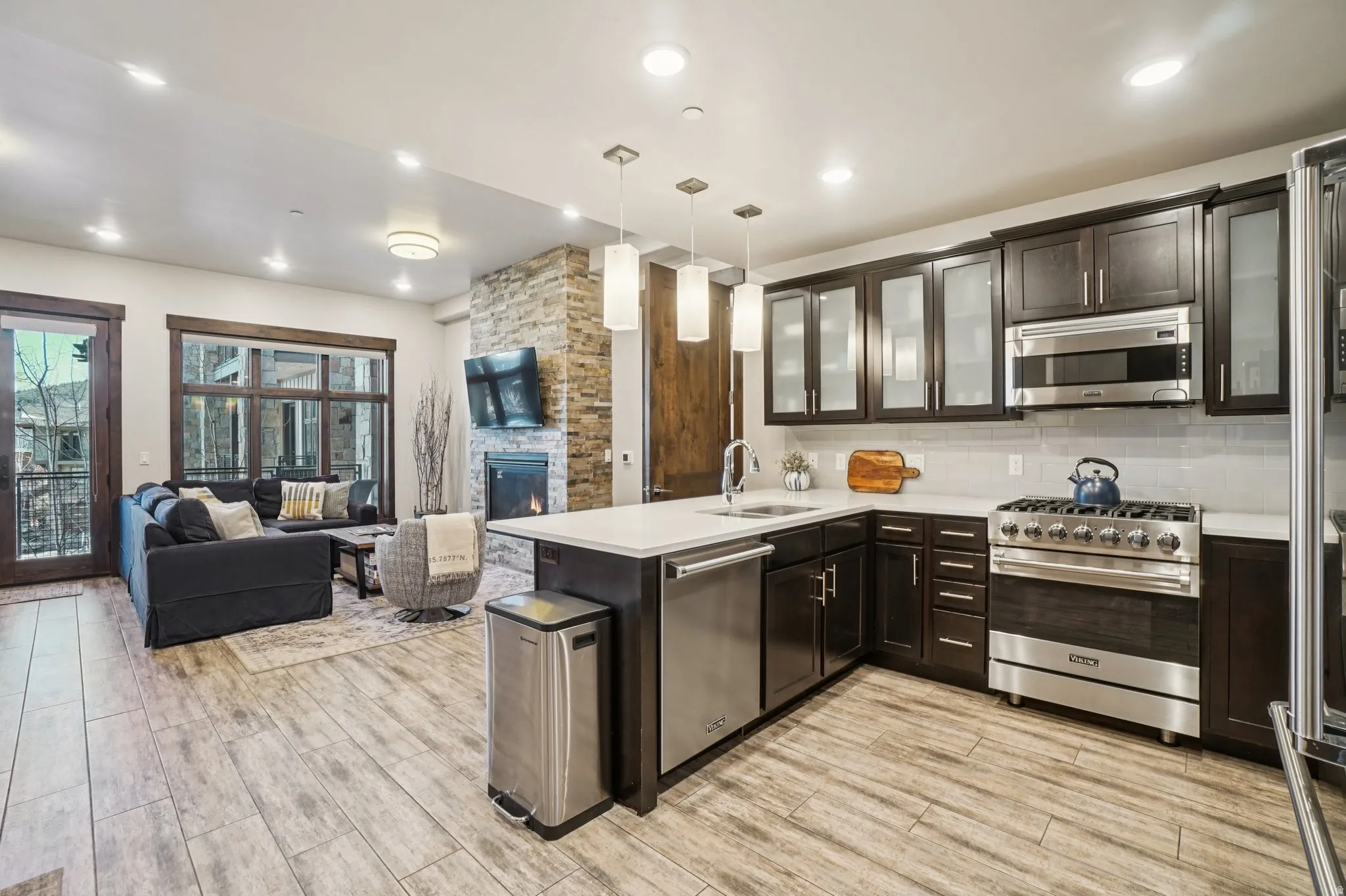 Kitchen with hanging light fixtures, high end appliances, glass insert cabinets, open floor plan, and light wood-type flooring