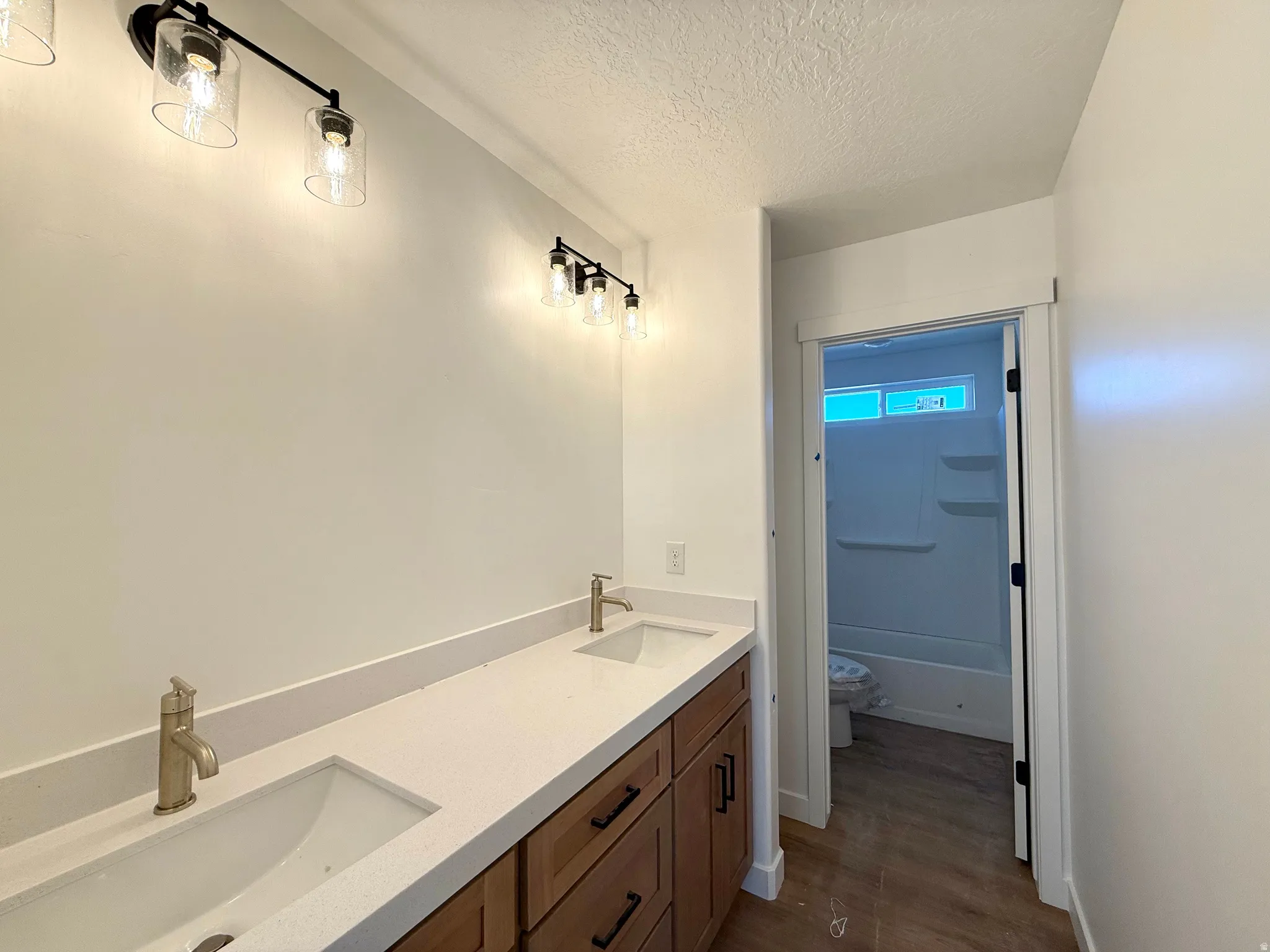 Bathroom featuring double vanity, a textured ceiling, and dark wood-style floors