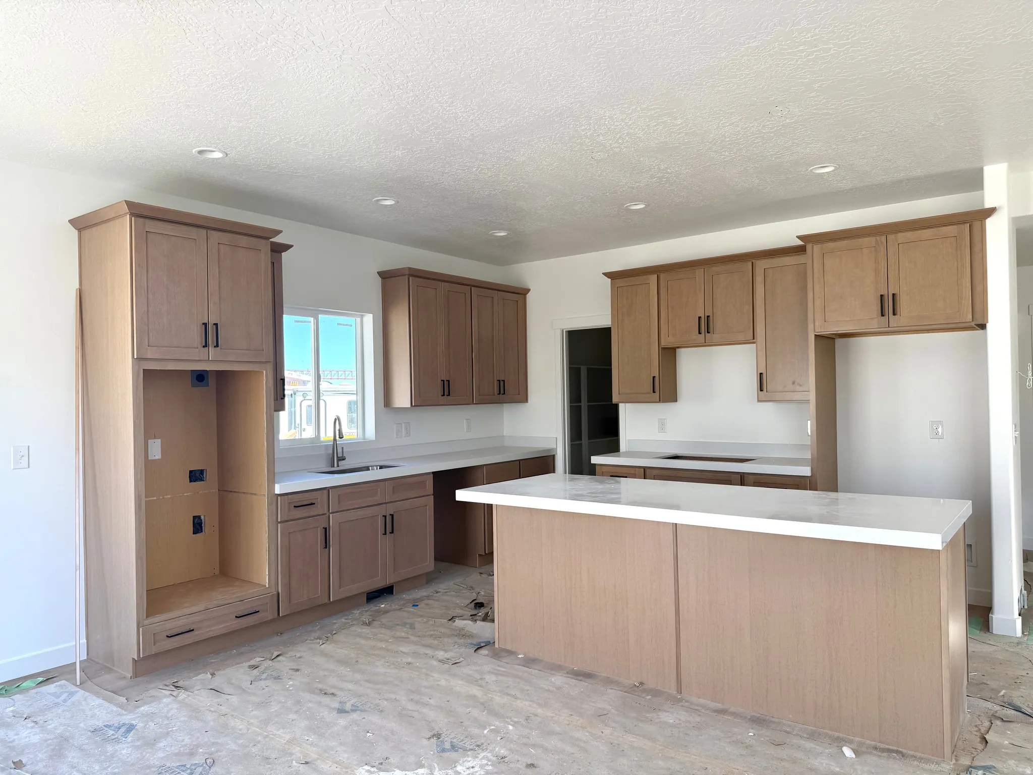 Kitchen featuring a kitchen island, wood finish cabinetry, recessed lighting, light countertops, and a textured ceiling