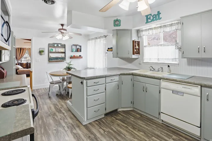 Kitchen featuring a peninsula, white dishwasher, dark wood-style flooring, a ceiling fan, and stainless steel microwave