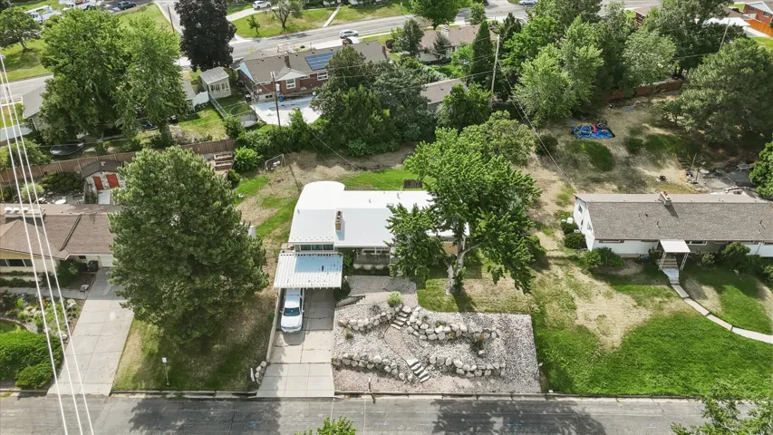 Property featuring an attached carport, terraced rock landscaping, mature trees, and a concrete driveway