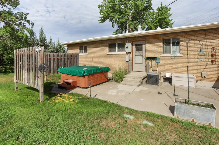 Spacious backyard patio featuring a hot tub, brick exterior, and mature trees