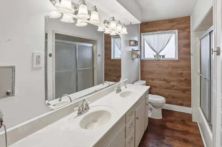 Full bath with wooden walls, a stall shower, double vanity, dark wood-style flooring, and a chandelier