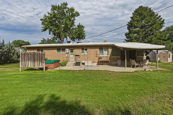 Expansive backyard featuring a manicured lawn, brick exterior, covered patio, concrete patio, and a storage shed