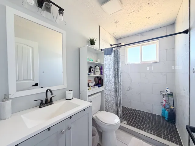 Bathroom featuring a vanity with an integrated sink, framed mirror, vanity lighting, a walk-in shower with tile surround, and a window