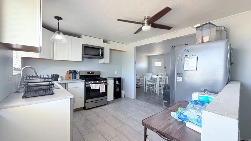 Kitchen featuring white cabinetry, stainless steel appliances, a ceiling fan, a pendant light fixture, and tile flooring