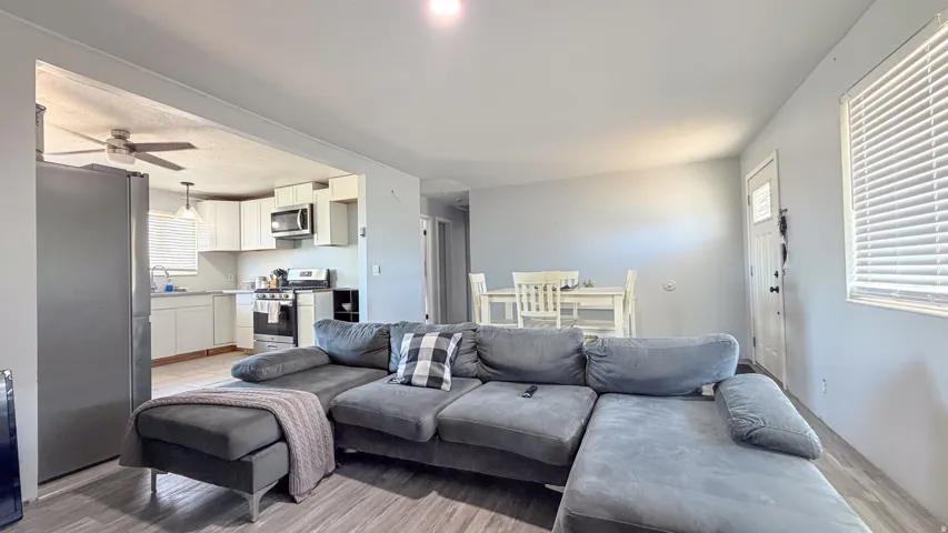 Wood-finish flooring throughout, kitchen with white cabinetry, ceiling fan, and stainless steel appliances