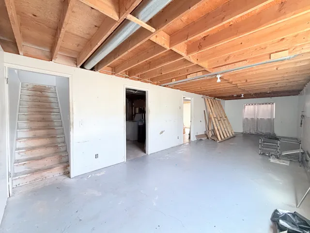 Unfinished basement offering exposed ceiling joists, concrete flooring, and a window opening with light-filtering curtains