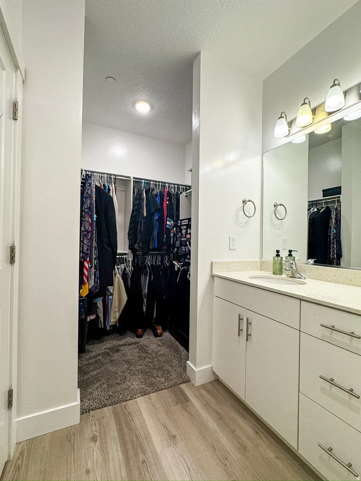 Bathroom featuring a spacious closet, vanity, a textured ceiling, and light wood-style flooring