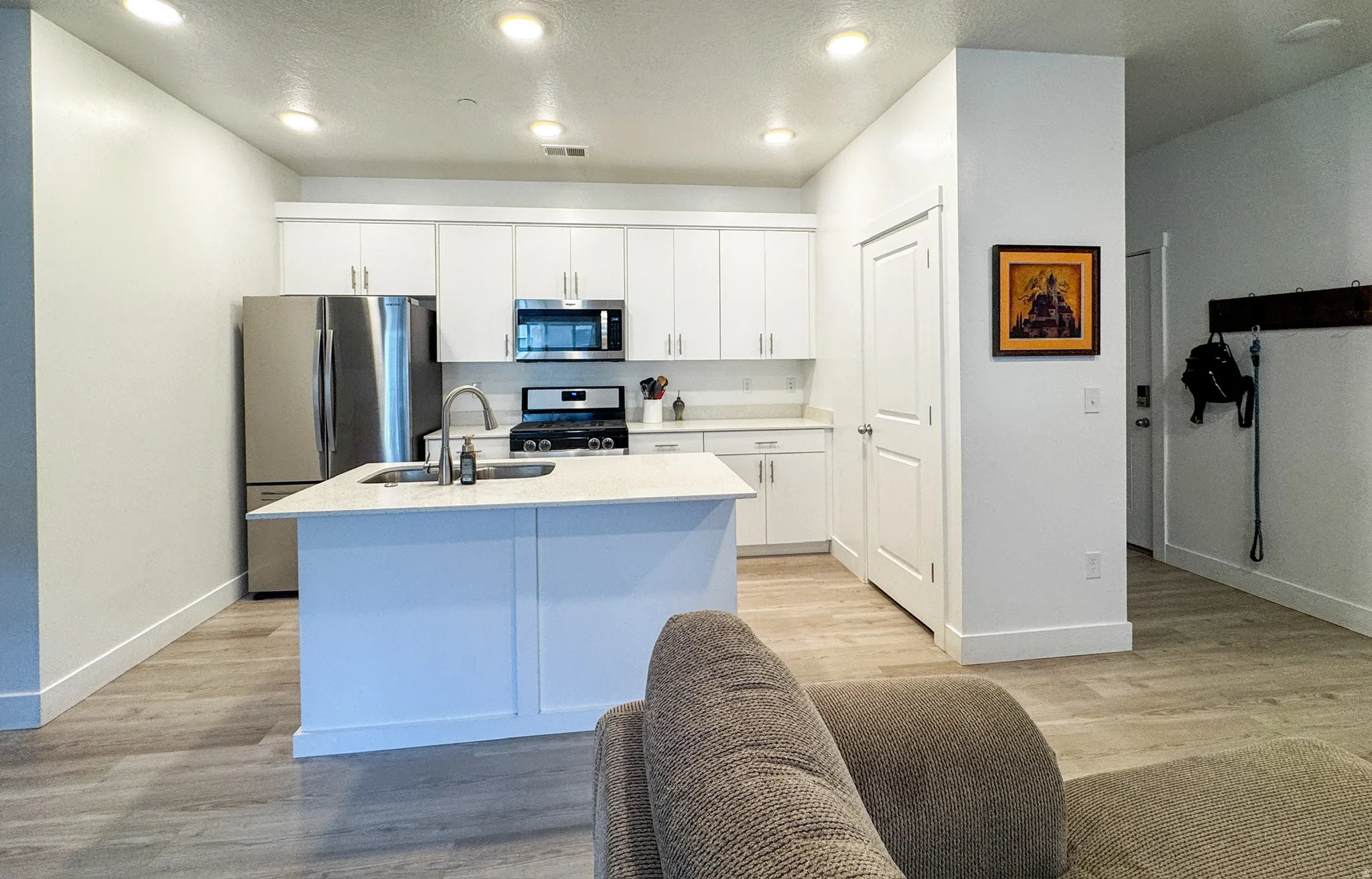 Kitchen with appliances with stainless steel finishes, light wood finished floors, white cabinets, a kitchen island with sink, and recessed lighting
