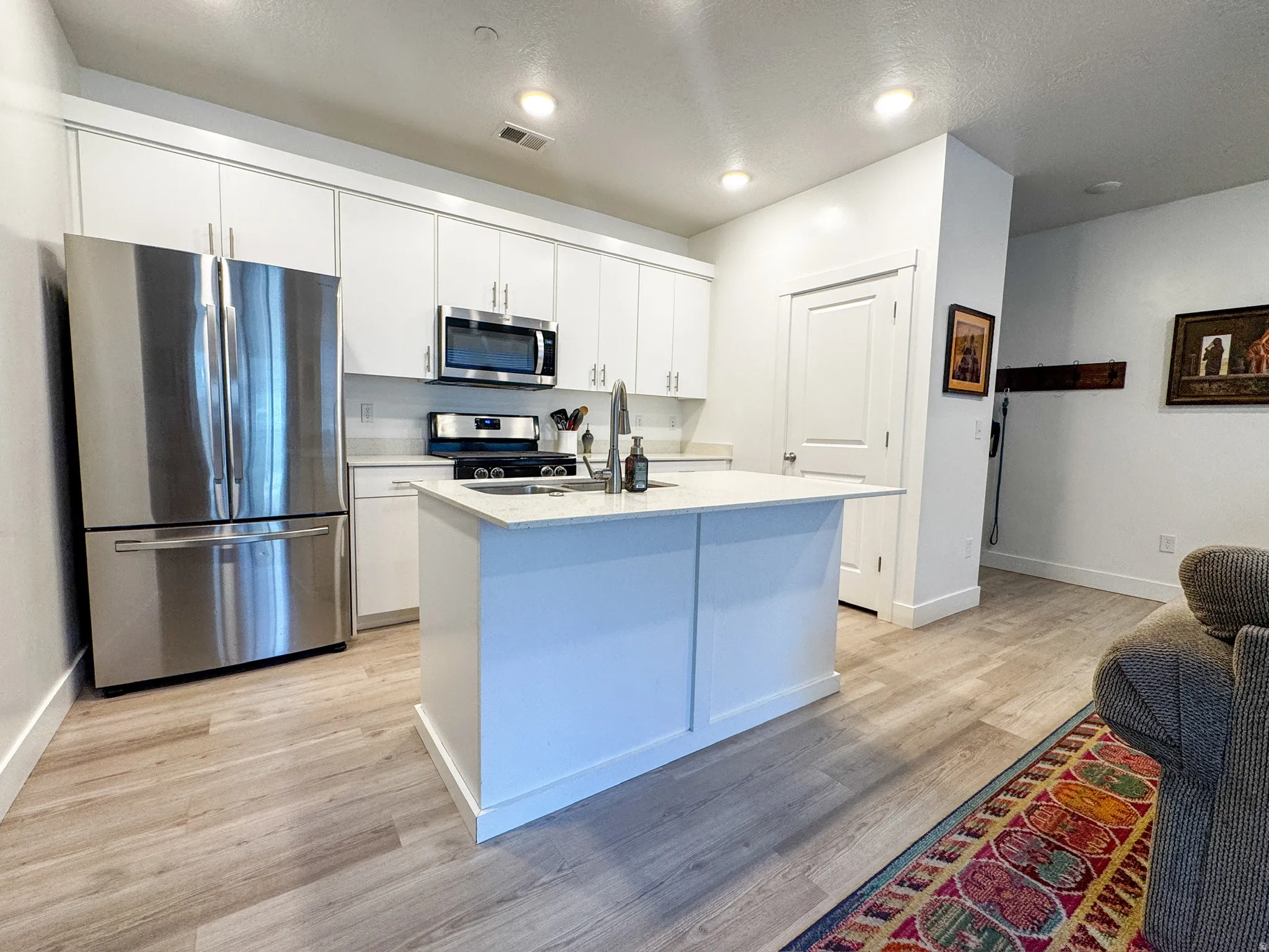 Kitchen featuring appliances with stainless steel finishes, light wood-type flooring, a center island with sink, white cabinets, and light stone counters