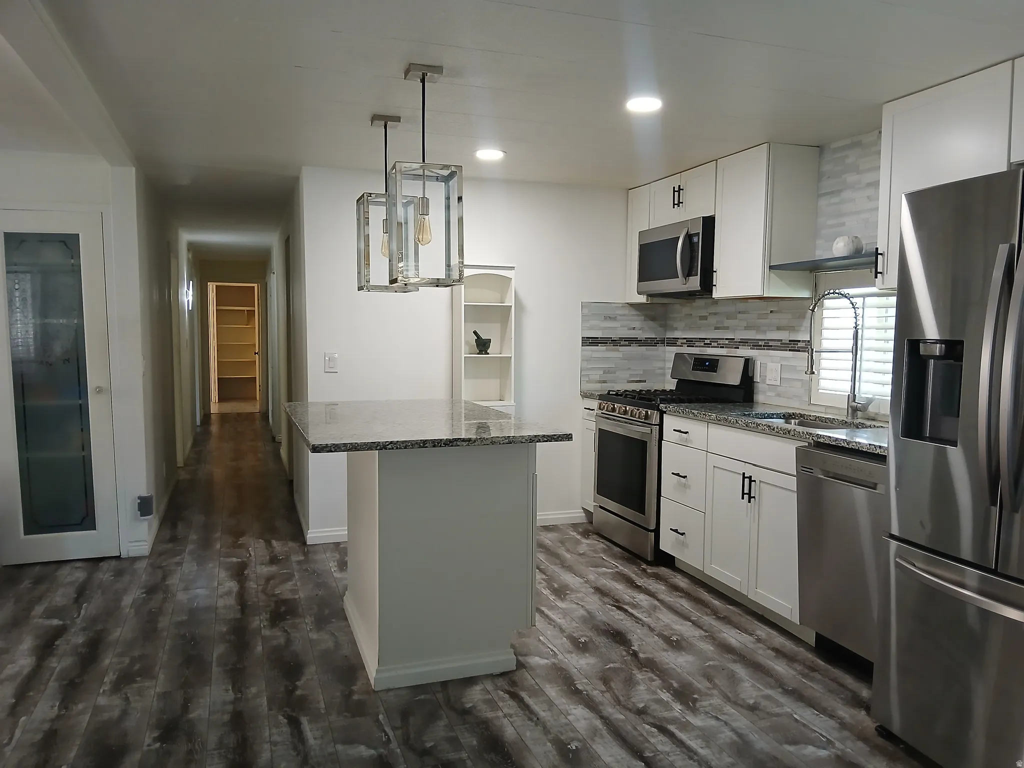 Kitchen with stainless steel appliances, white cabinetry, dark stone counters, decorative backsplash, and hanging light fixtures