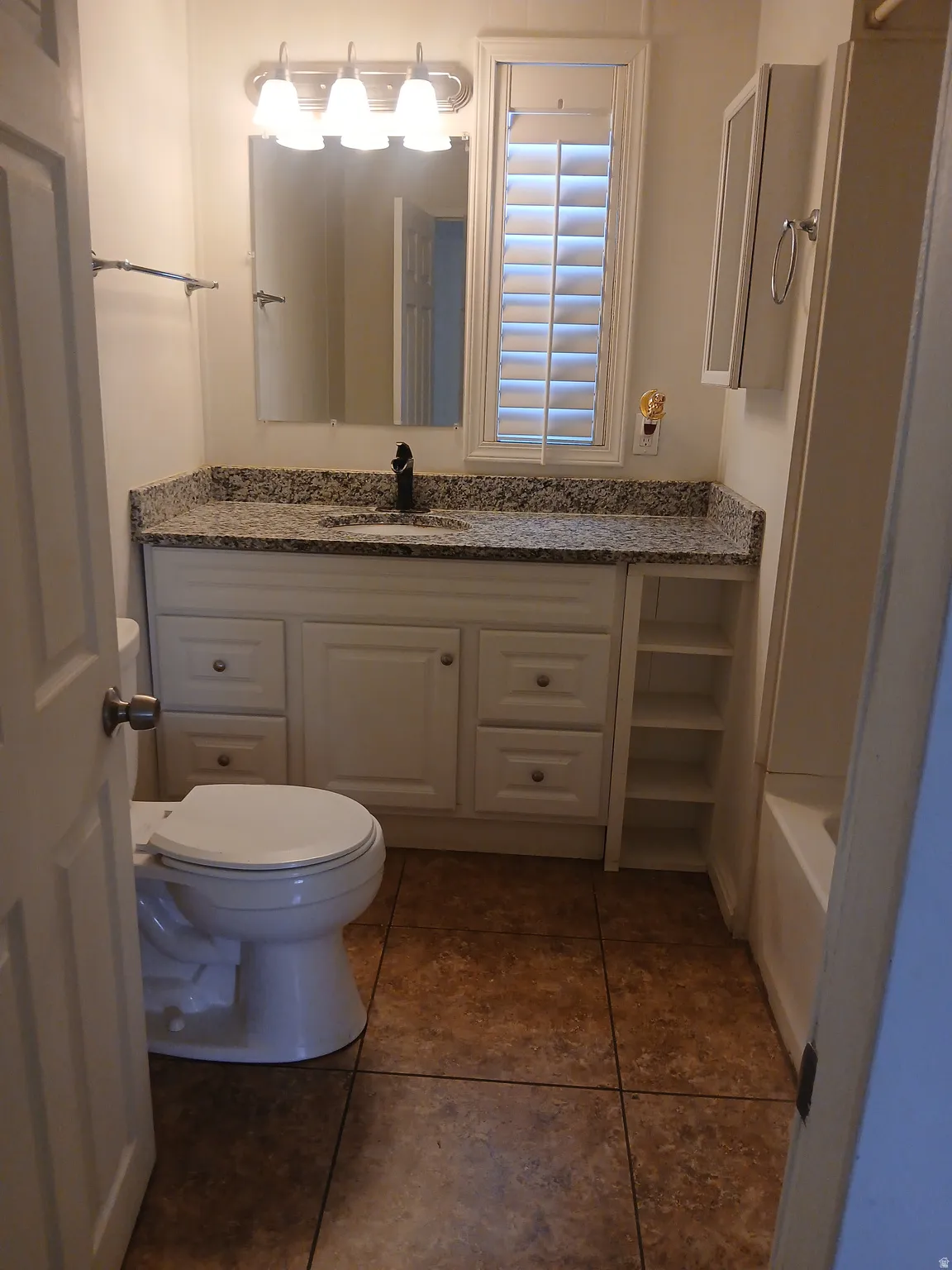 Bathroom featuring vanity, dark tile patterned flooring, and  shower combination
