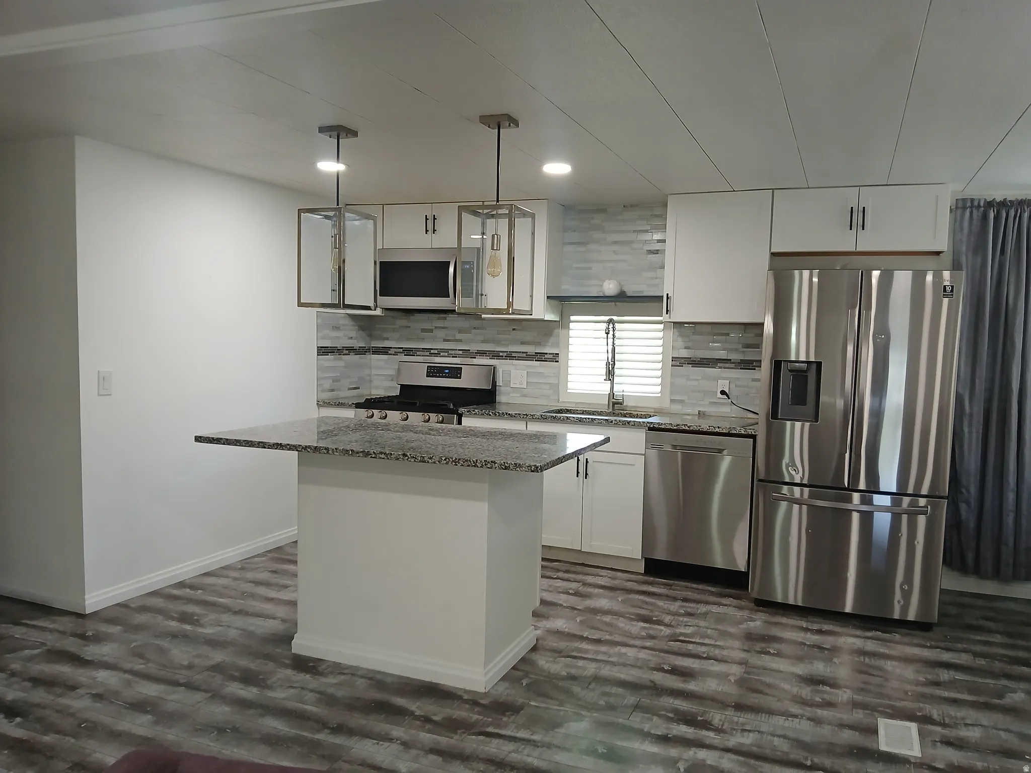 Kitchen with light stone countertops, stainless steel appliances, white cabinets, decorative light fixtures, and recessed lighting