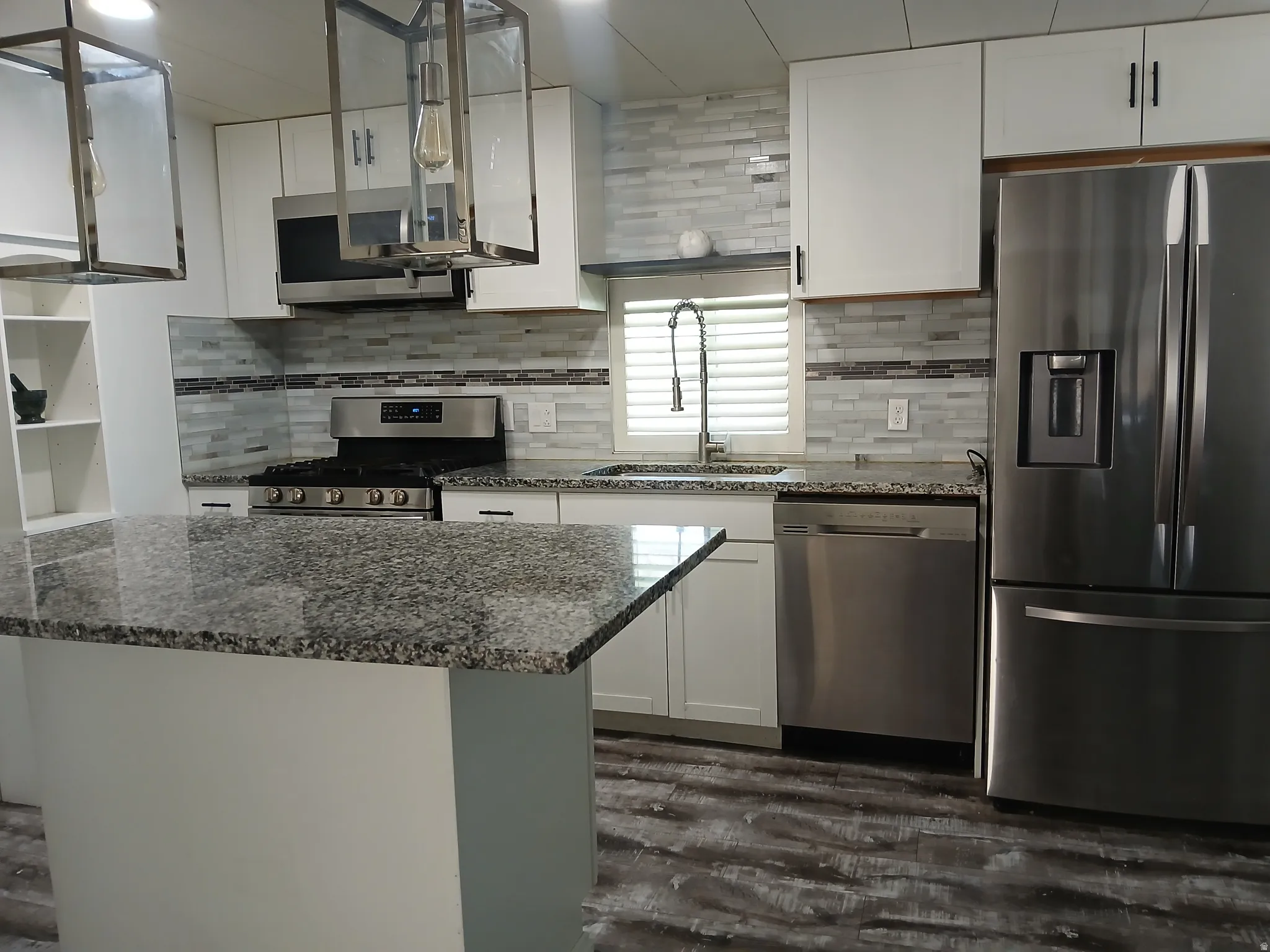 Kitchen featuring appliances with stainless steel finishes, dark stone countertops, white cabinetry, and dark wood-type flooring