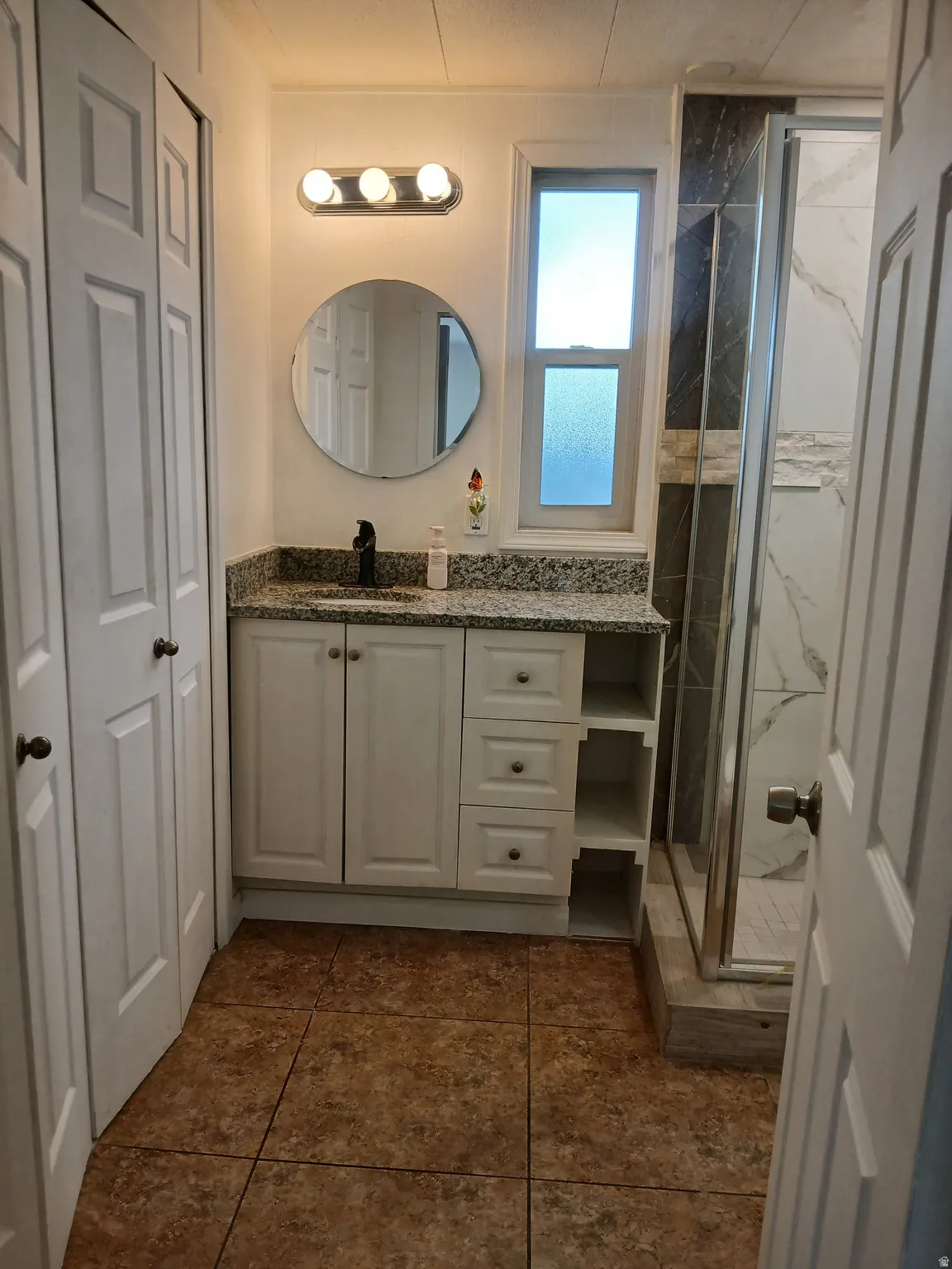 Full bathroom with vanity, a marble finish shower, a closet, and dark tile patterned flooring