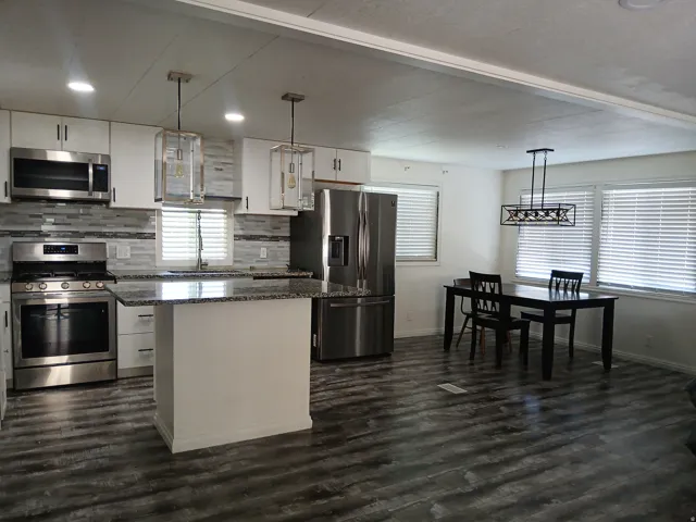 Kitchen featuring hanging light fixtures, appliances with stainless steel finishes, white cabinetry, a kitchen island, and tasteful backsplash