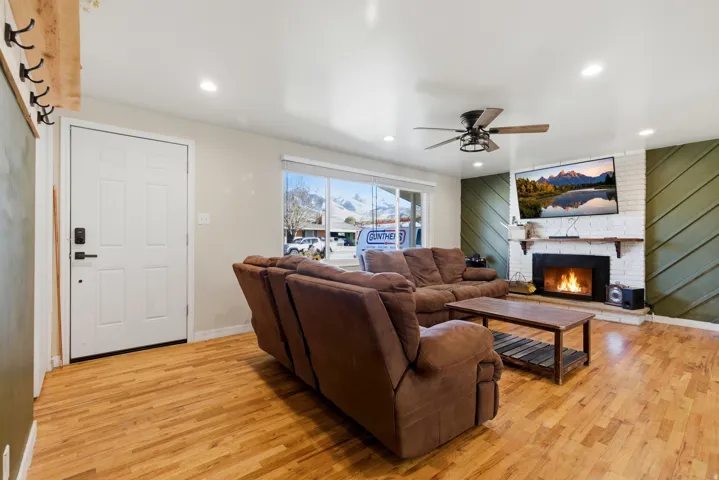 Living room featuring light wood-style flooring, a fireplace, a ceiling fan, and recessed lighting