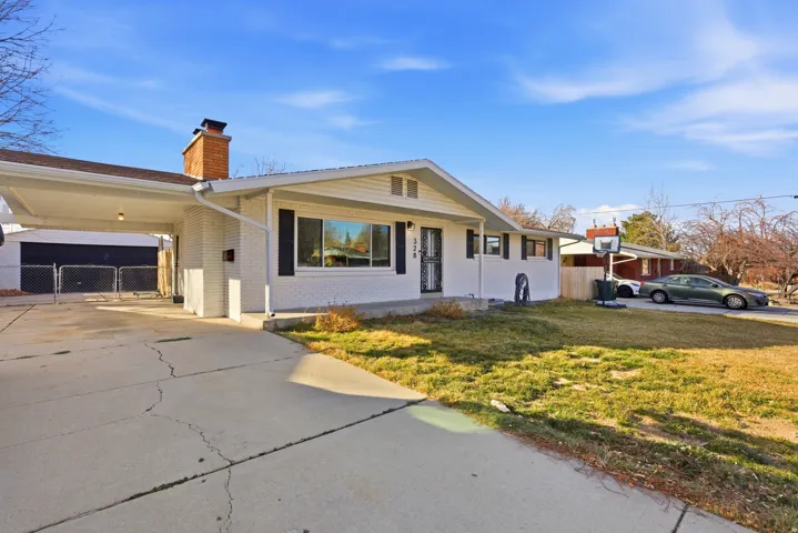 Single story home featuring brick siding, a chimney, driveway, and an attached carport