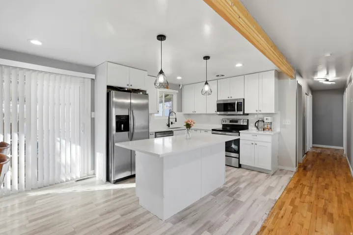Kitchen featuring appliances with stainless steel finishes, white cabinets, pendant lighting, a kitchen island, and light wood-style flooring