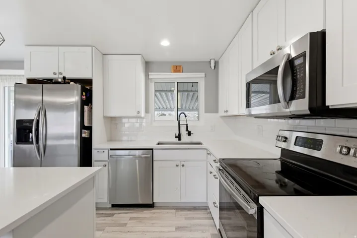 Kitchen with appliances with stainless steel finishes, white cabinets, light wood-type flooring, light stone countertops, and backsplash