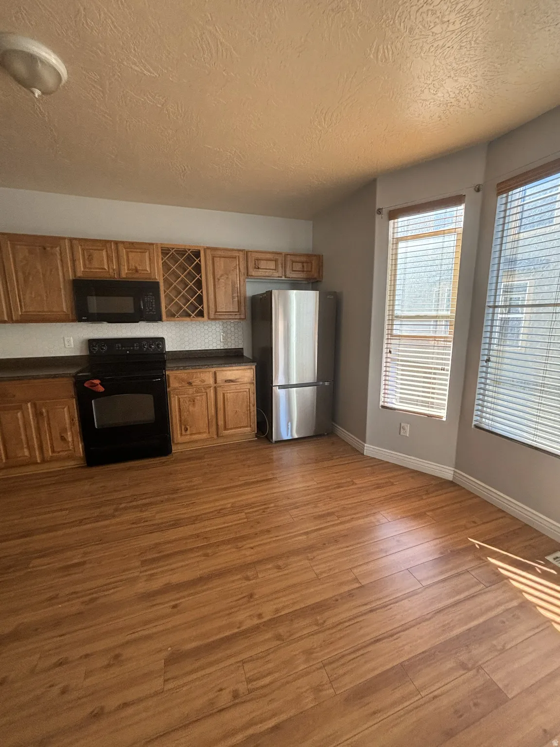 Kitchen featuring dark countertops, black appliances, brown cabinetry, a textured ceiling, and light wood-style flooring