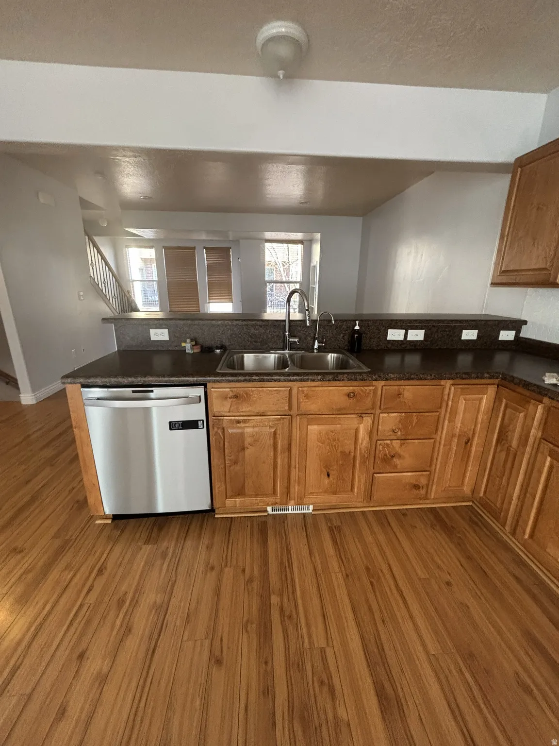 Kitchen featuring brown cabinets, dishwasher, dark wood-style floors, and dark stone countertops