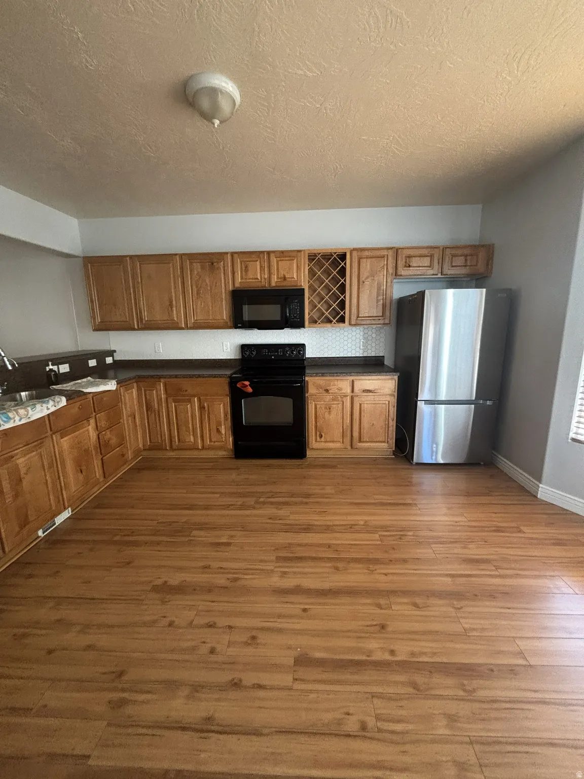 Kitchen with black appliances, brown cabinetry, dark wood-style floors, a textured ceiling, and decorative backsplash
