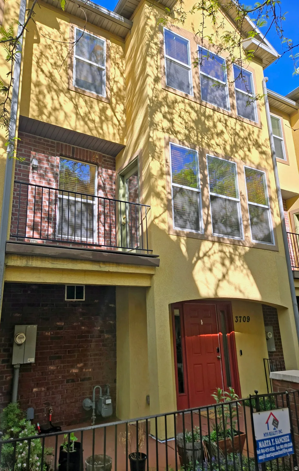 View of front of house with a balcony, brick siding, stucco siding, and a fenced front yard