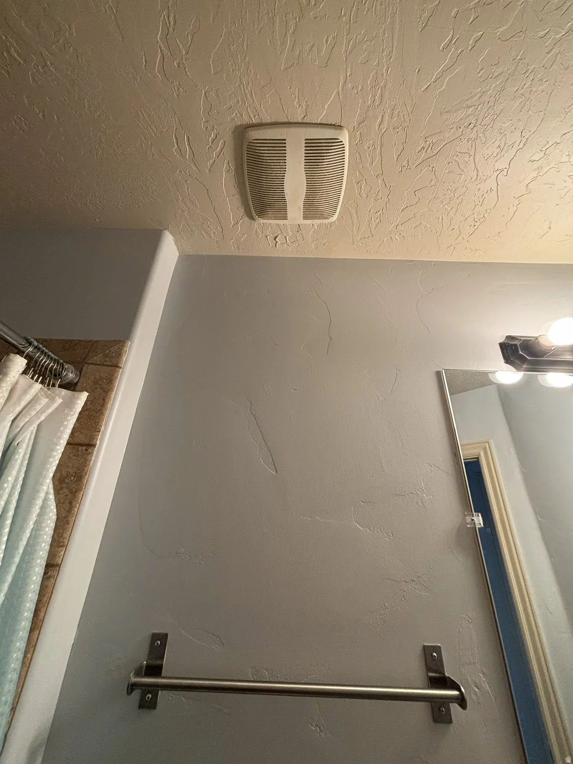 Bathroom view of a textured ceiling, curtained shower, and a textured wall