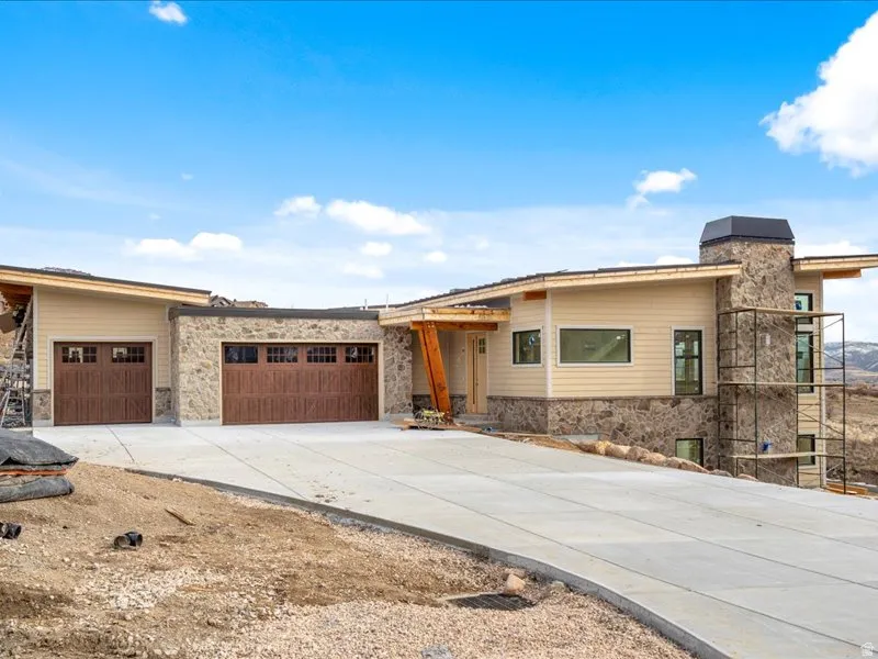 View of front of house featuring stone siding, concrete driveway, a garage, and a chimney