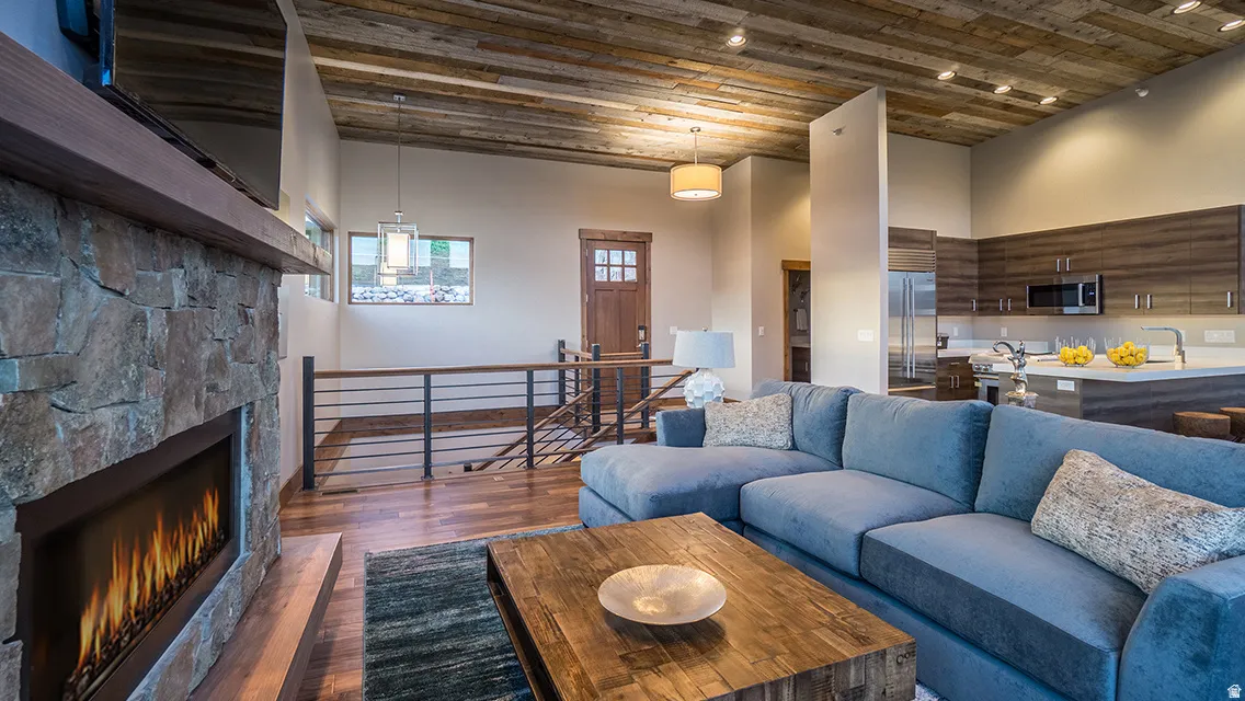 Living area with a stone fireplace, dark wood-style floors, a high ceiling, and wooden ceiling
