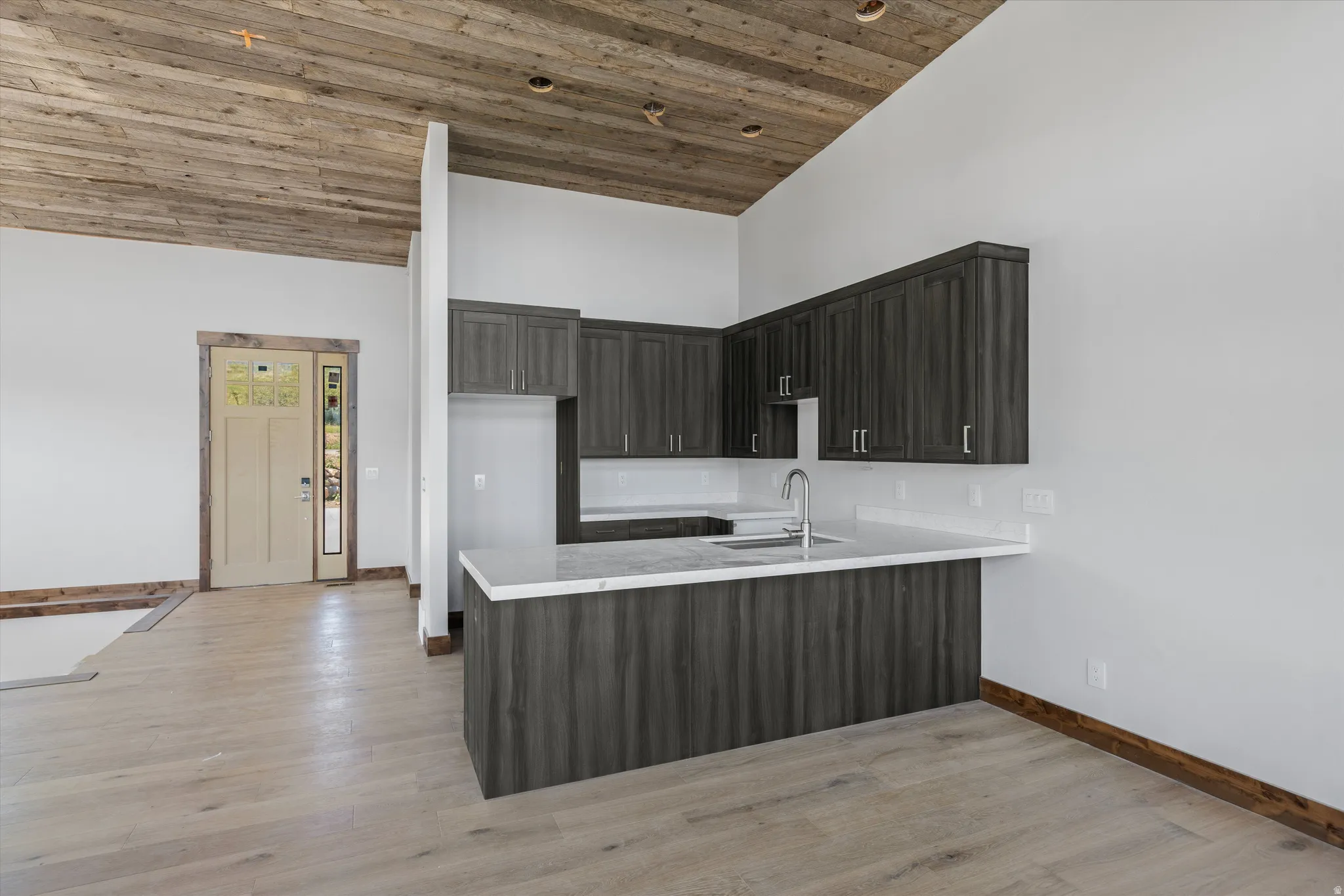 Modern kitchen area featuring dark wood-finish cabinetry, light countertops, and a stainless steel sink with a gooseneck faucet