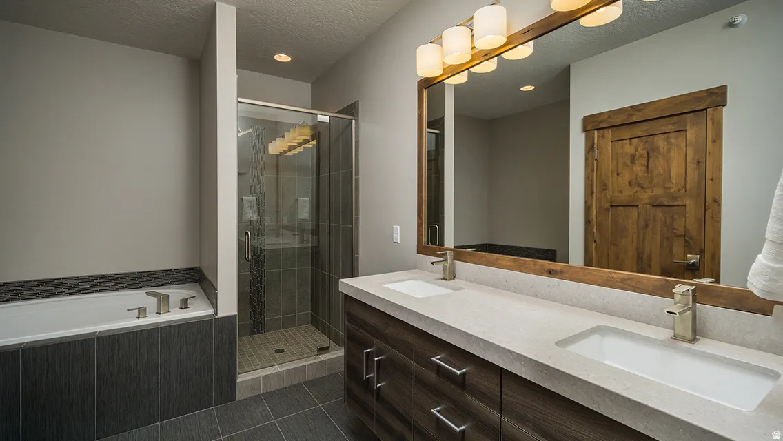 Full bathroom with double vanity, a shower stall, a bath, a textured ceiling, and recessed lighting