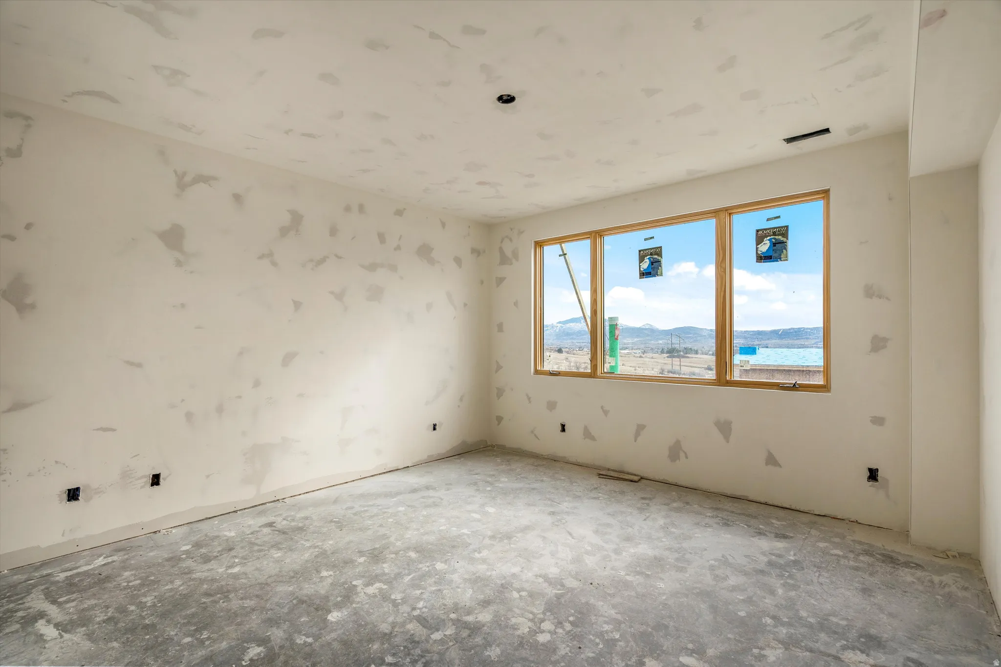 Spacious room with large multi-pane window, wood-finish window frames, and plaster-ready wall surfaces