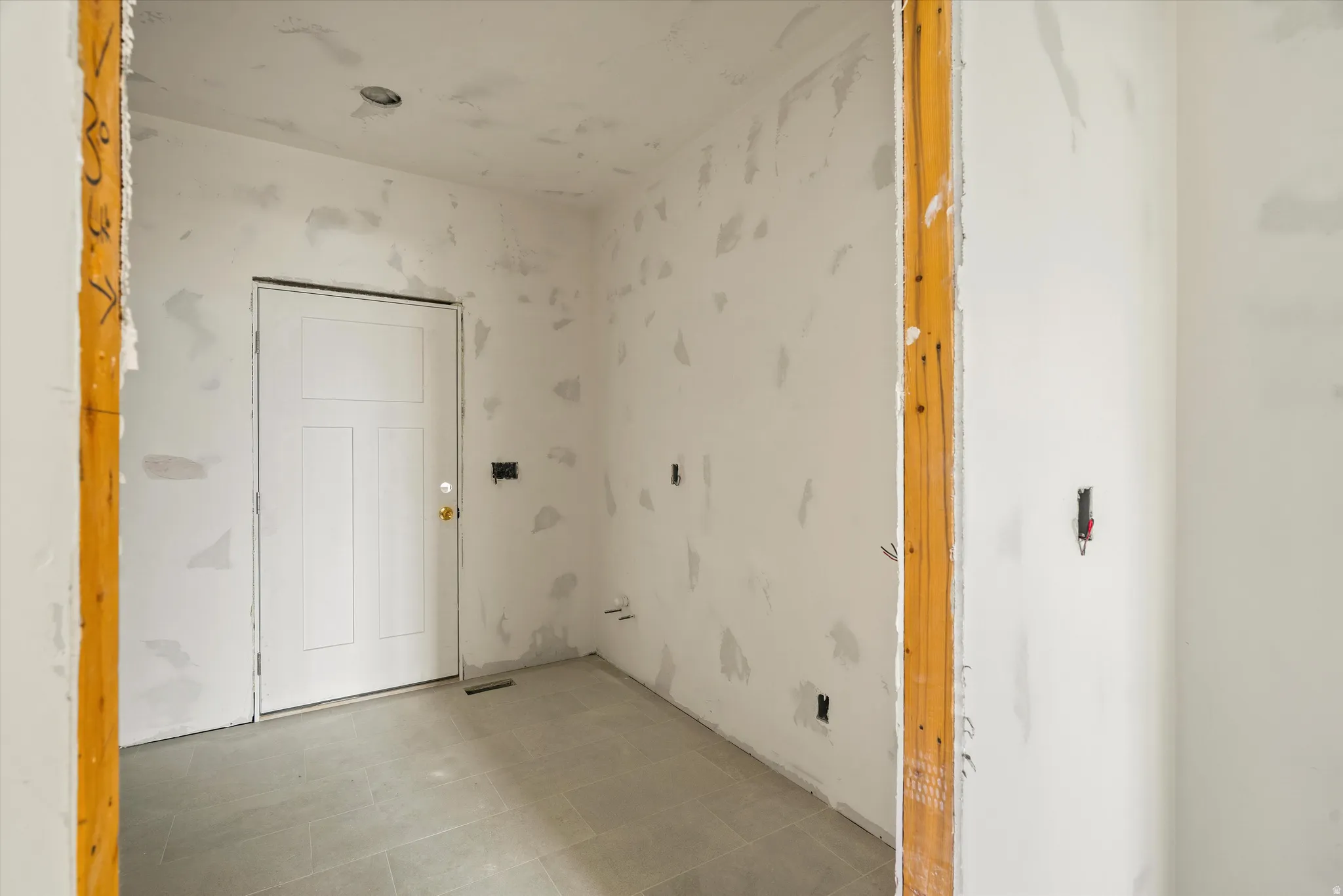 Interior space featuring gray tile flooring, a white paneled door with brass hardware, and recessed lighting