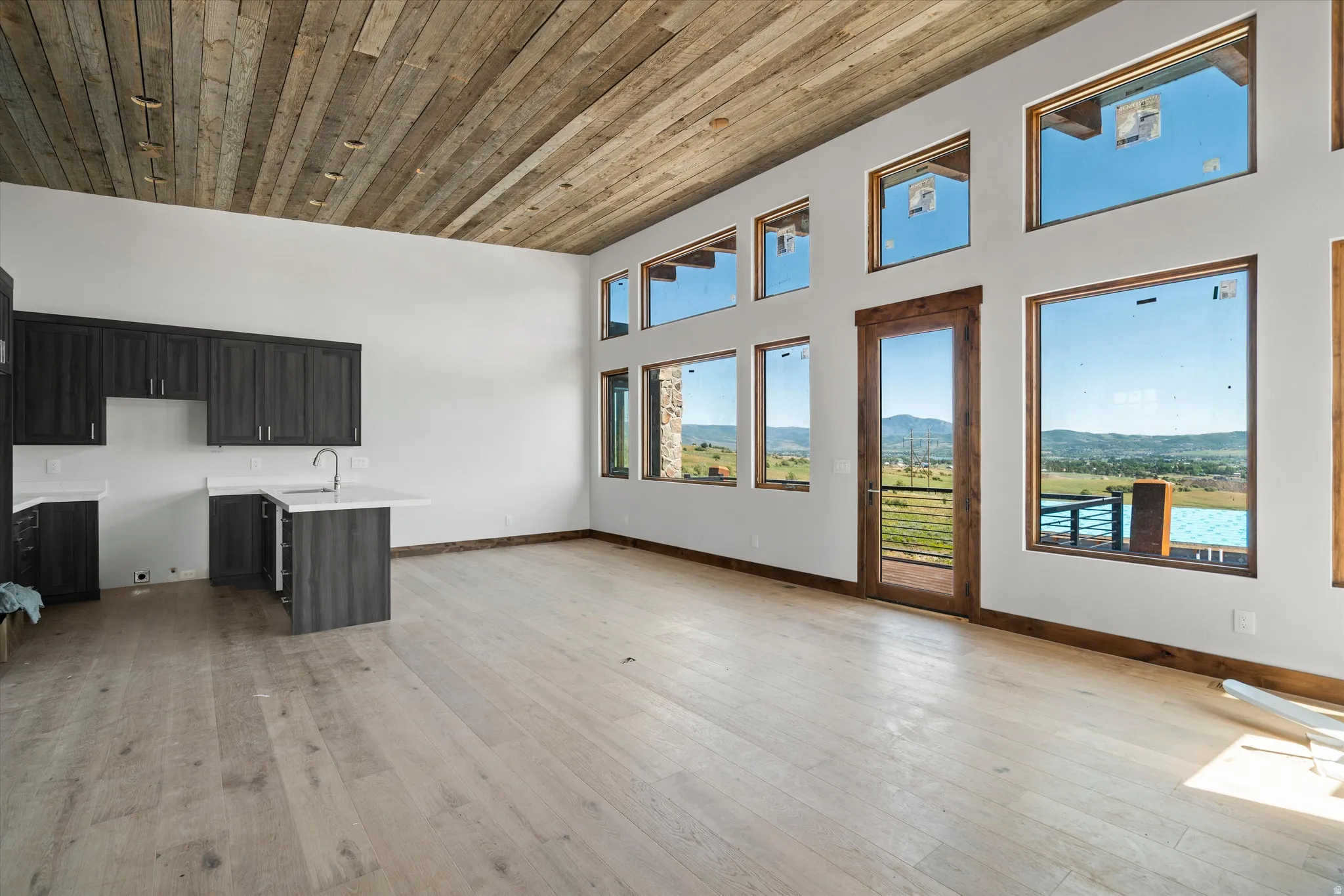 Spacious open concept room featuring a natural wood plank ceiling, light wood-finish flooring, and a wall of assorted windows with dark wood trim